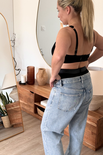Frau steht vor dem Spiegel und schaut sich in Shapewear Klamotten an
