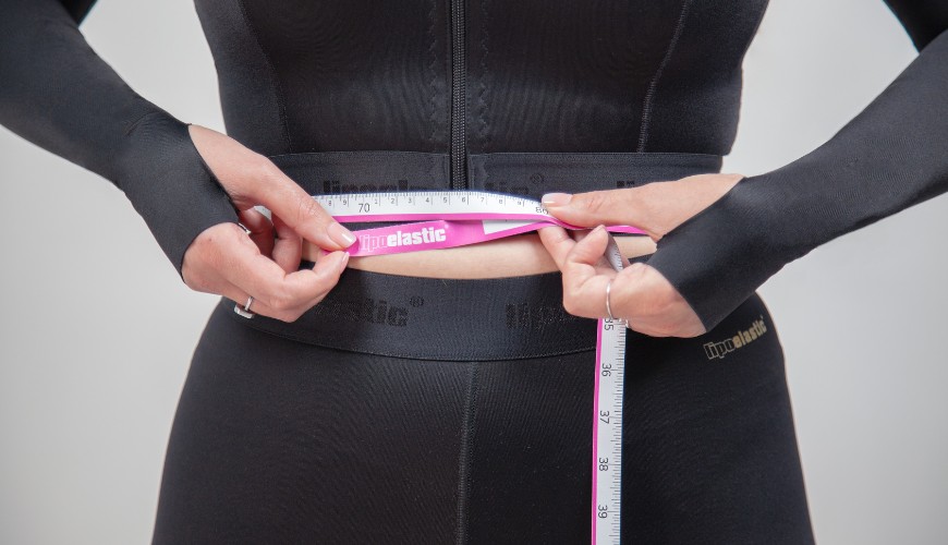 Eine Frau, die Kompressionsmieder trägt, nimmt mithilfe eines Maßbandes eigene Maße, um passende Größe des Mieders zu bestimmen.