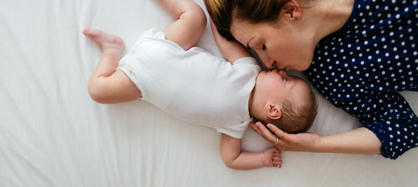 Mutter mit ihrem Baby, liegen gemeinsam im Bett, sie küsst es liebevoll